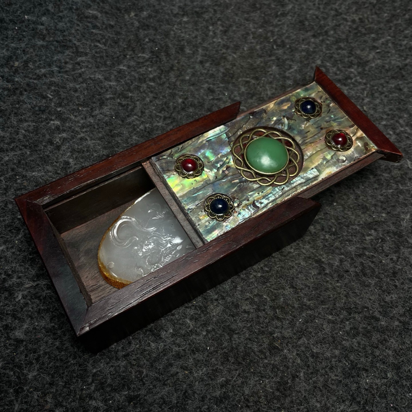 A white jade pendant is placed inside a rosewood inlaid with colorful shells box