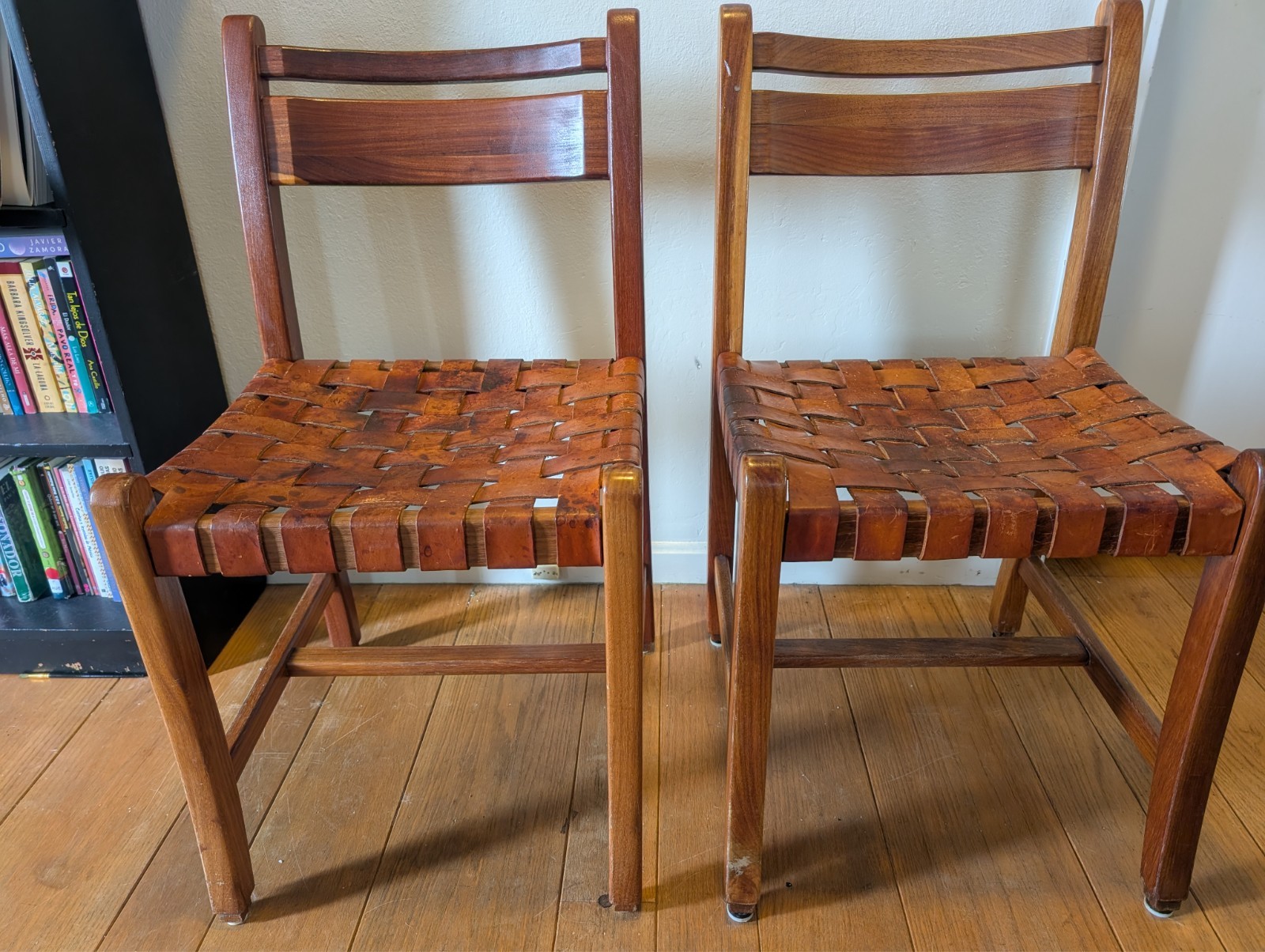 two mid century wooden chairs with leather straps for seating